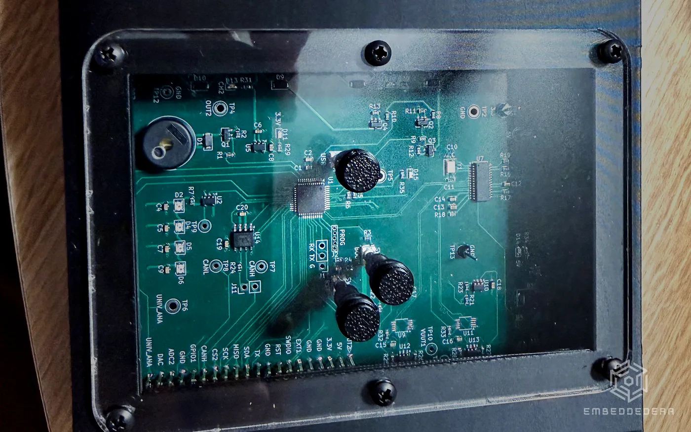 One of our test fixtures seen from above: a black enclosure with a screwed-down acrylic window, the board inside pressed by spring probes.